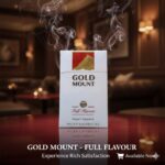 ซองบุหรี่ Gold Mount Red แบบซองแข็ง วางบนโต๊ะไม้สีเข้มในบรรยากาศเลาจน์สุดหรู มีควันลอยละล่องสื่อถึงความเข้มข้นของรสชาติ