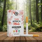 บุหรี่ THIS Africa Mola Random Five ซองสีขาวลายกราฟิกรูปสัตว์และผลไม้ วางคู่กับมวนบุหรี่ก้นกรองสีส้มบนโต๊ะไม้ ฉากหลังป่า