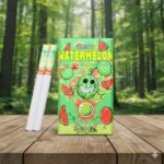 บุหรี่ Zest Watermelon ซองสีเขียวลายกราฟิกแตงโมพร้อมมวนบุหรี่เม็ดบีบ วางบนโต๊ะไม้ฉากหลังป่าสีเขียว